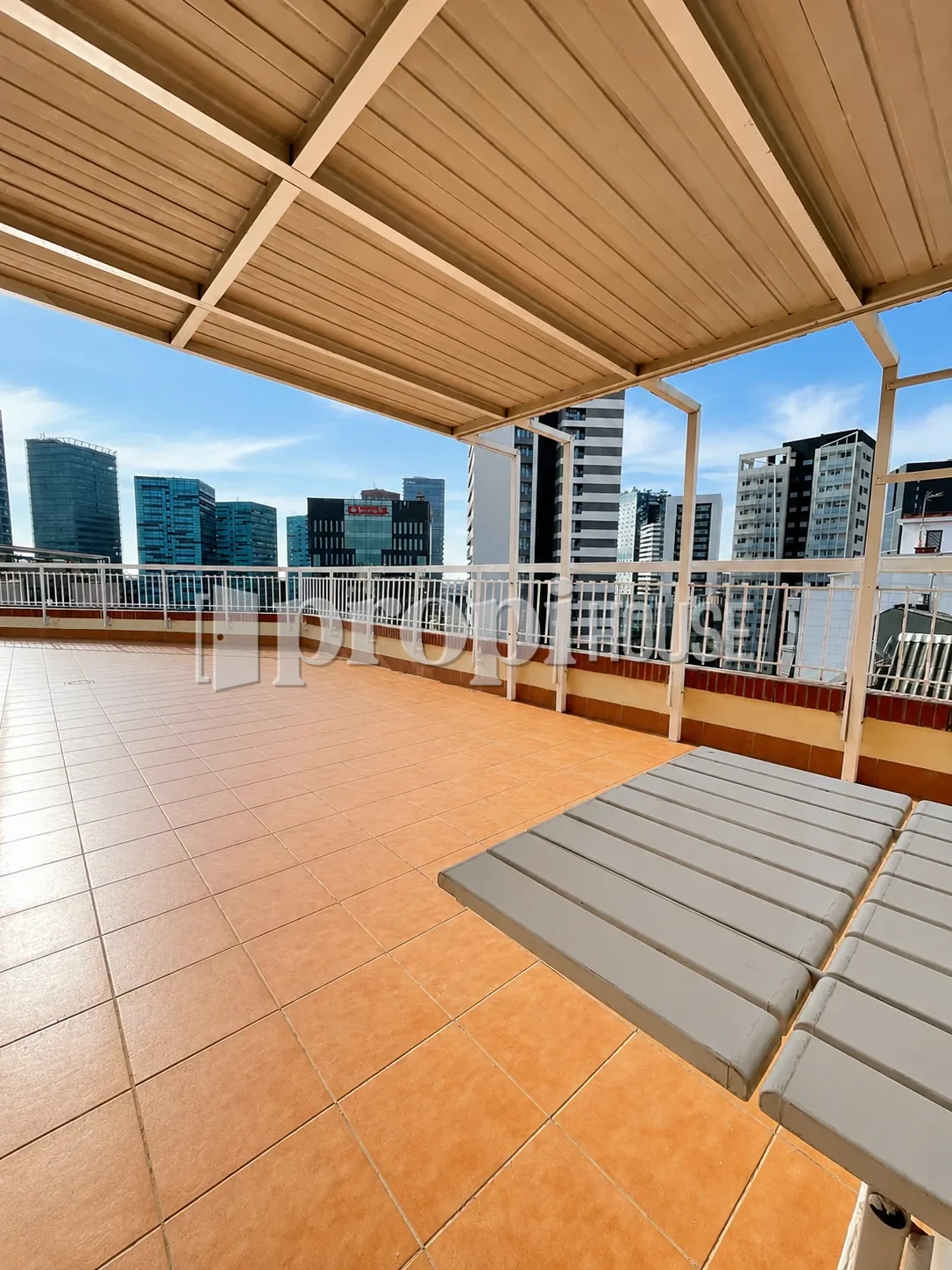 Terraza del ático bajo la pérgola, con las torres de Plaza Europa al fondo